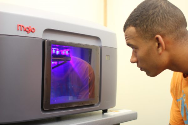 Jordan Venters '18 peers into the 3D printer as it creates a prototype of one of the Introduction to Engineering Design class projects. (Photo by Jessica Meis ’19)