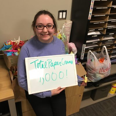 Katie Hohman '18 holds a sign reading "total paper cranes: 1,000."