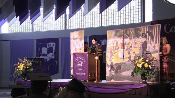 Professor Christina Penn-Goetsch speaks during Commencement with an art installation on the stage. 