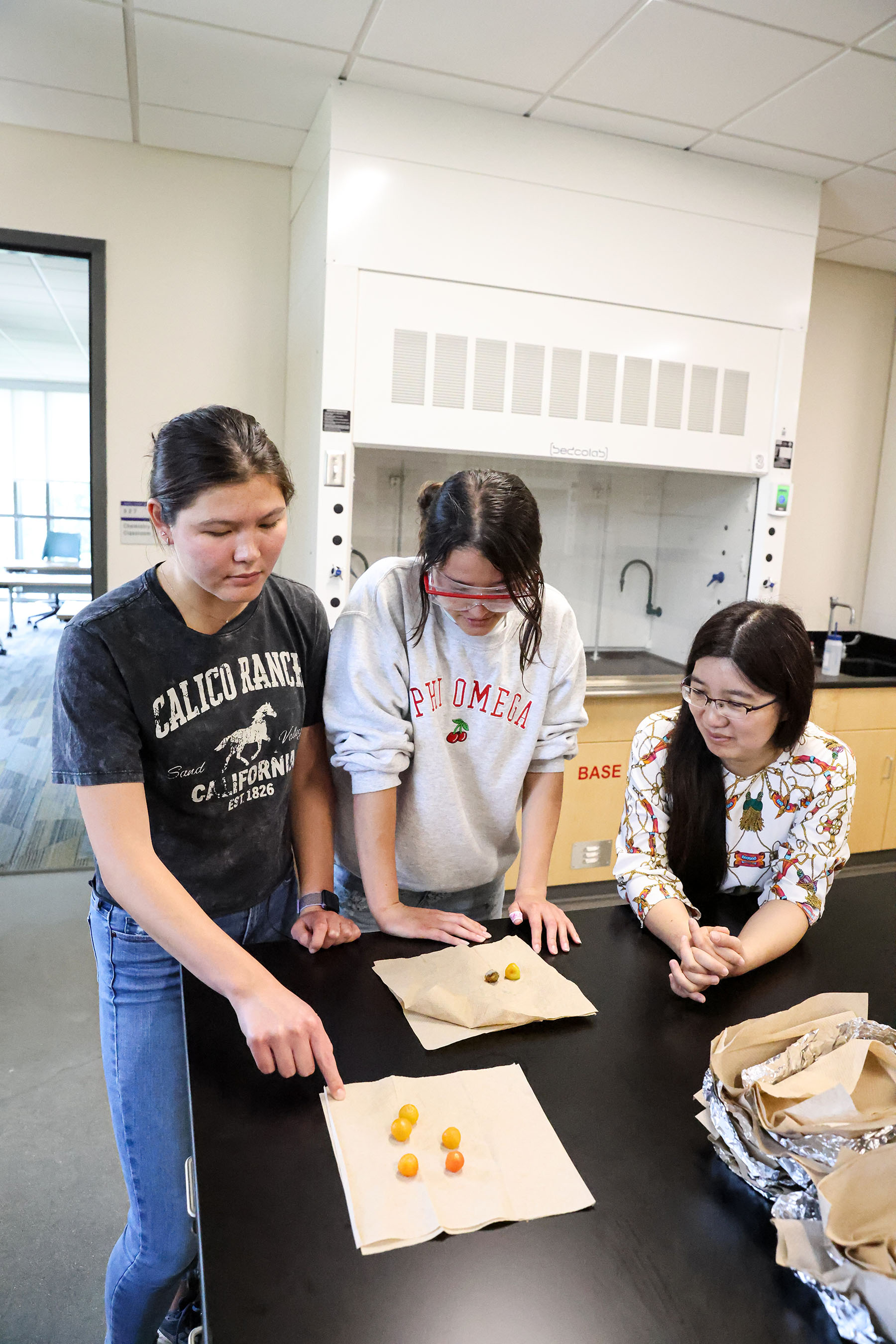 Two students looking at the ripening stages of tomatoes with their professor in a lab setting.