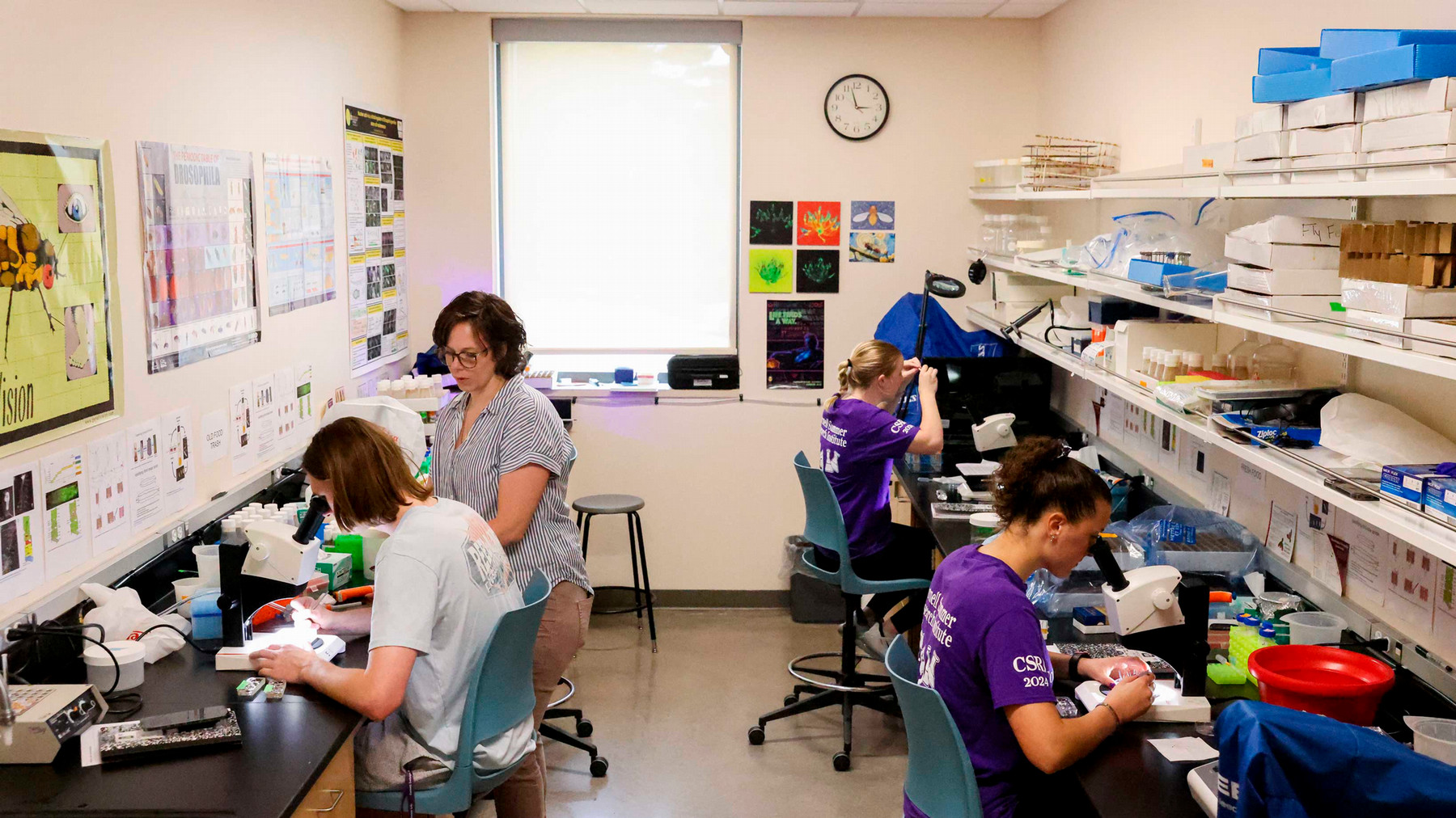 Three students work on microscopes with their professor in a science lab.