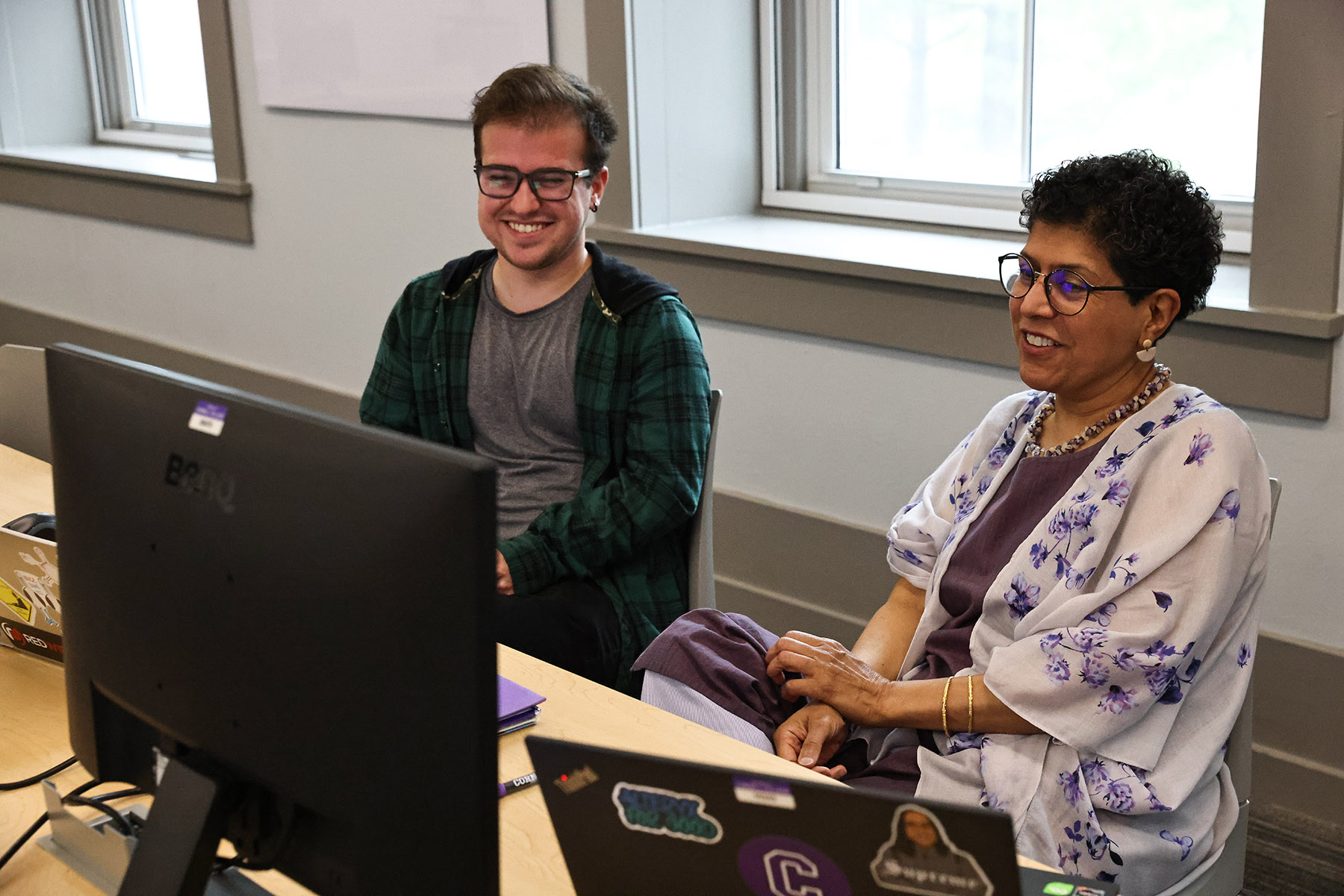 Student and Professor sitting in front of computer monitors smiling.