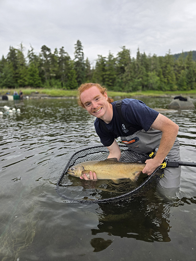 Lewis in a stream holding a large fish.
