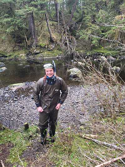 Lewis standing by a stream in scuba gear to keep warm.