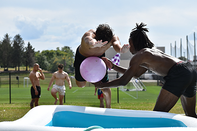 One student tags another with a big purple ball on a slip-n-slide