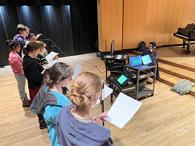 Students standing in front of audio recording equipment as they record a script.