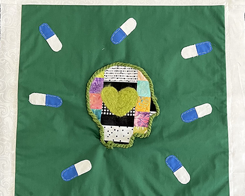 A quilt with pills and a person's head depicted with a heart.