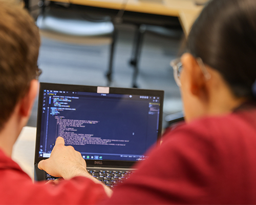 A computer with digits and a student pointing with the screen.