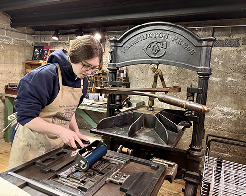 Sophia Dohmen ‘28 inks the forme—a locked arrangement of type—before printing the cover of a chapbook on the 19th-century Washington iron hand press. 