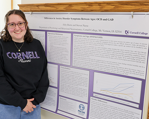 Abby Burns '25 stands next to a paper she co-authored with Professor Steven Neese.