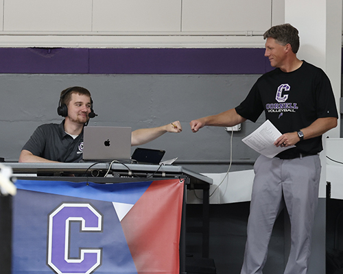 Jack Carlson '26 and Assistant Director of Athletics for Communications Kerry Kahl fist bump at the September 3, 2025 volleyball match against Dubuque.
