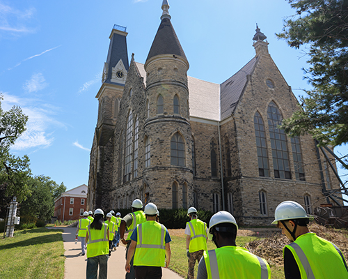 Students wearing bright yellow vests and hard hats walk to King Chapel.