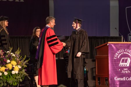 Mackenzie Crow '18 with President Jonathan Brand. They are on the stage shaking hands during graduation.