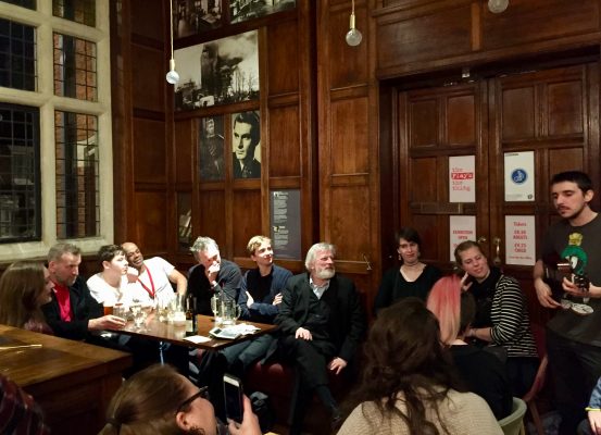 Students and actors gather around a table at a nearby bar.