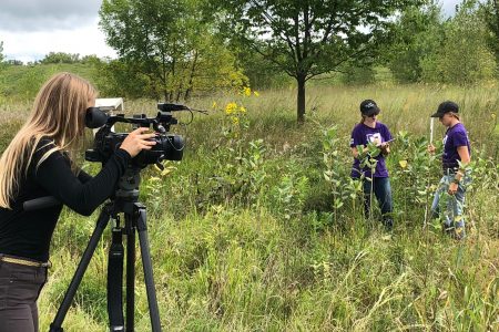 A photographer takes video of students working in the prairie