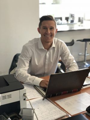 Ethan Berube smiling for the camera while sitting at his desk