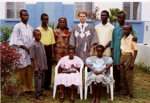 Craig Vickstrom ’92 (center) still visits the family he lived with in Ghana. Members of the family are seen with him in front of their home; the seated girls are now bankers.