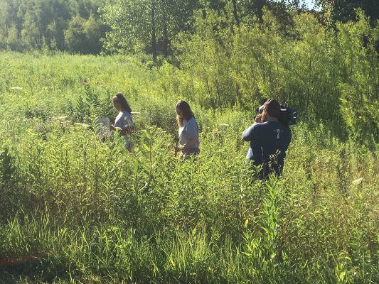 Photographer taking video of students doing research in an Iowa prairie