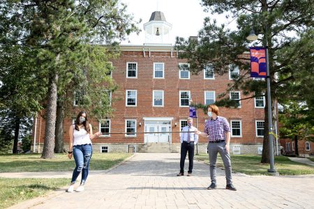 Cornell seniors Paulina Diaz-Alton and Jack Bressett demonstrate the use of a 6-foot-and-two-hands stick, with President Jonathan Brand standing behind them.  College Hall, built in 1857, was built when the sticks were in use to keep student couples apart.