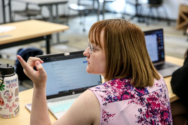 Student sits in front of a computer and points to the white board