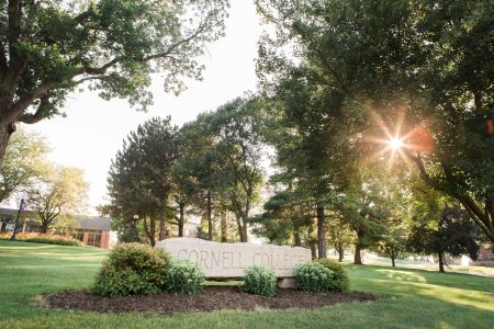 Sun shines through the trees behind the Cornell College sign