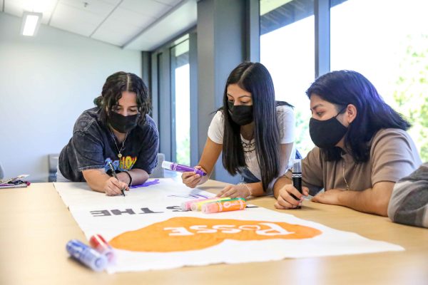 Three students work on a poster using large markers