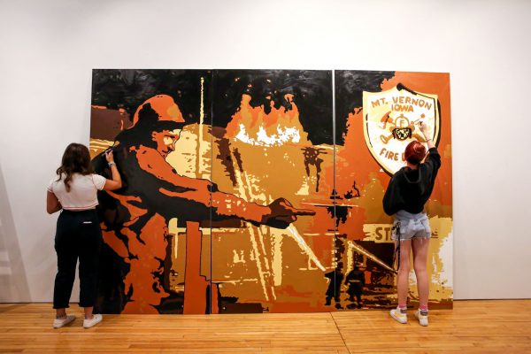 Two students painting on a large mural of a firefighter