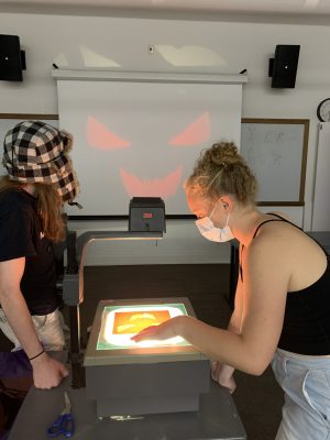 Two students work to create a spooky face on a projector.