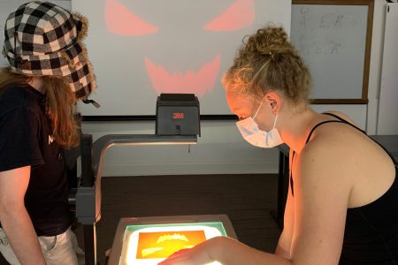 Two students work to create a spooky face on a projector.