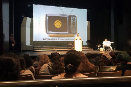 Students sit in the audience and listen to a speaker on stage