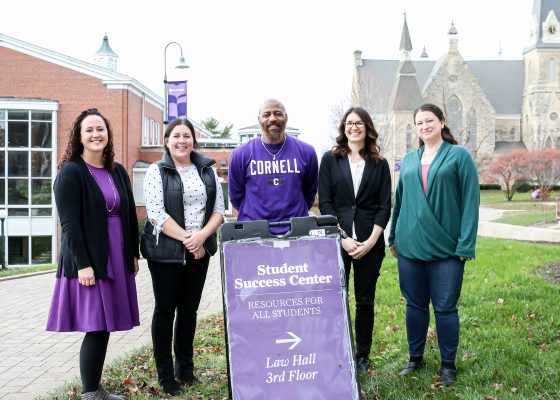 Five staff members on the student success team stand by a sign that reads "Student Success Center" on the Ped Mall on the Cornell College campus