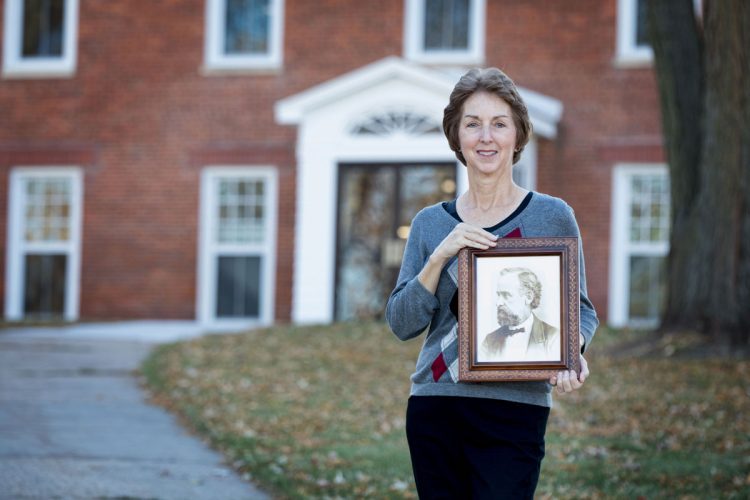 Bonnie Dodge '76 stands in front of Old Sem holding a photo of her 2nd great-granduncle, David H. Wheeler, who taught in that building when it opened in 1853.