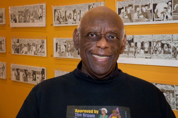 Rupert Kinnard ’79 in Peter Paul Luce Gallery, McWethy Hall, with some of his cartoons behind him, before his artist’s reception.