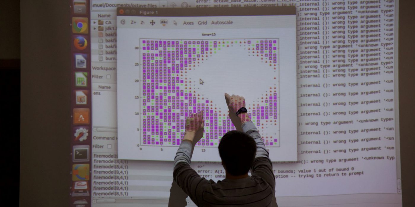 Student pointing to screen on the board where a projector is showing his data for a research project