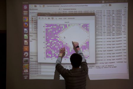 Student pointing to screen on the board where a projector is showing his data for a research project