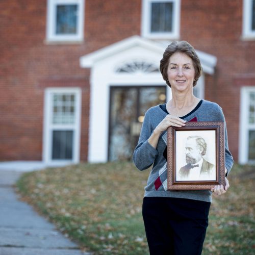 Bonnie Dodge ’76 stands in front of Old Sem holding a photo of her 2nd great-granduncle, David H. Wheeler, who taught in that building when it opened in 1853.