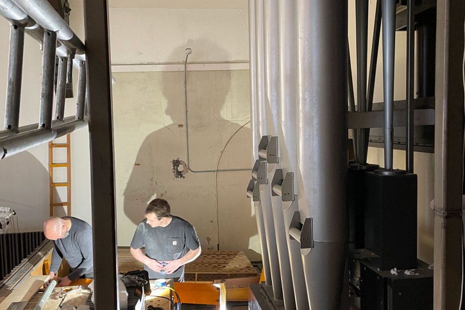 A worker and his teammates disassemble the 1967 pipe organ from its loft above the King Chapel stage, as his shadow hovers overhead.