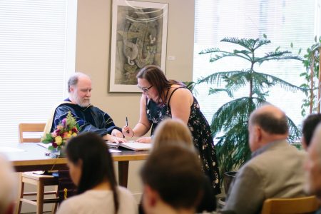 A Phi Beta Kappa initiate signs the historic ledger during initiation in 2018. Longtime Phi Beta Kappa Treasurer and Secretary Professor David Yamanishi looks on.