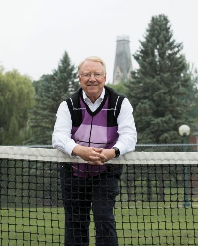 Fred Burke '70 poses at the tennis court with King Chapel in the background