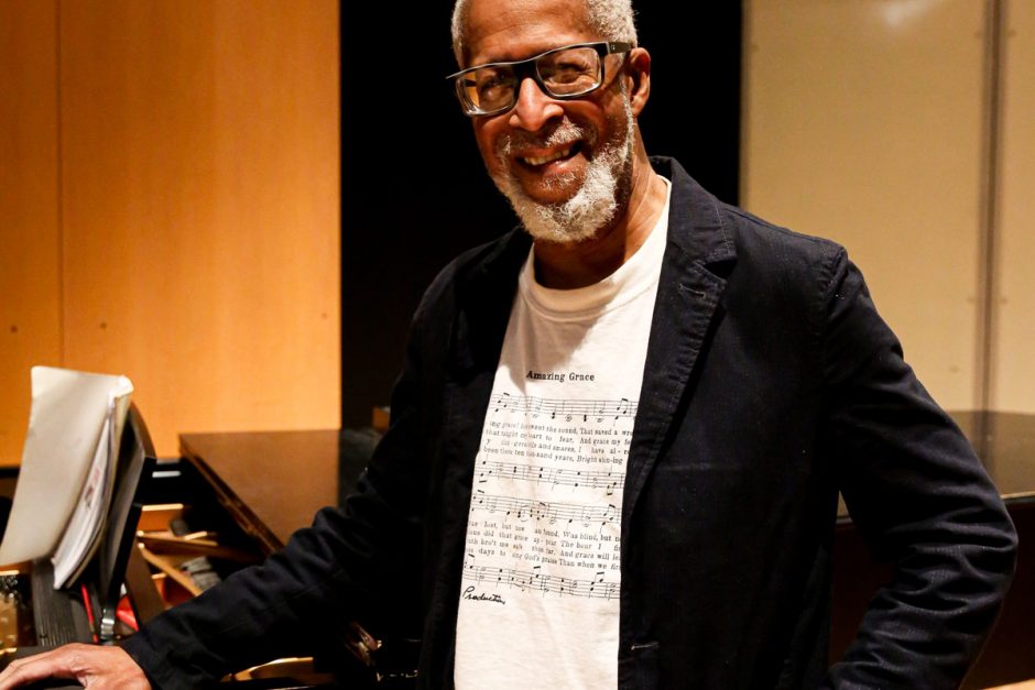 Wearing a musical score T-shirt and jacket, Charles Thomas Hayes '77 smiles at the camera prior to a choir rehearsal he led in Ringer Recital Studio.