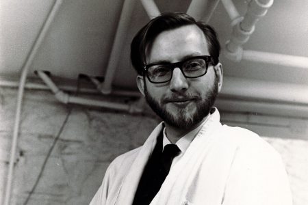 Black-and-white image of Professor Neil Wylie in a shirt, tie, and white lab coat.