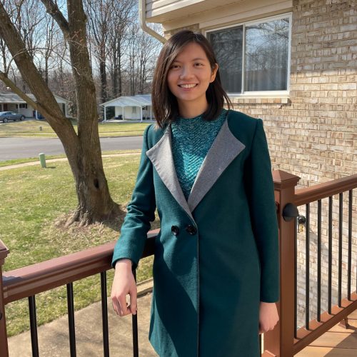 Trang Hoang ’15 stands outdoors in a teal sweater and coat.