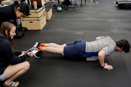 Two students watch as a third student does a plank on the floor.