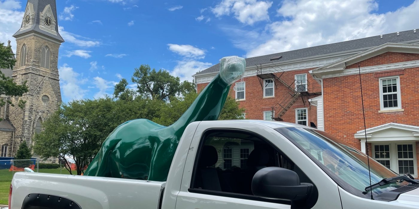 Sinclair dinosaur in the back of a white pickup truck with a Cornell College logo.