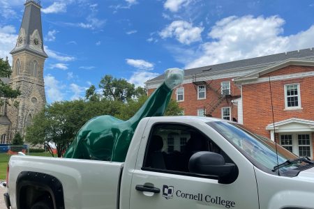 Sinclair dinosaur in the back of a white pickup truck with a Cornell College logo.