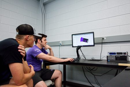 Two students sit in front of a computer looking at a design of a wind tunnel