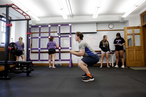 Josiah Shaw squatting while student record his progress in the background