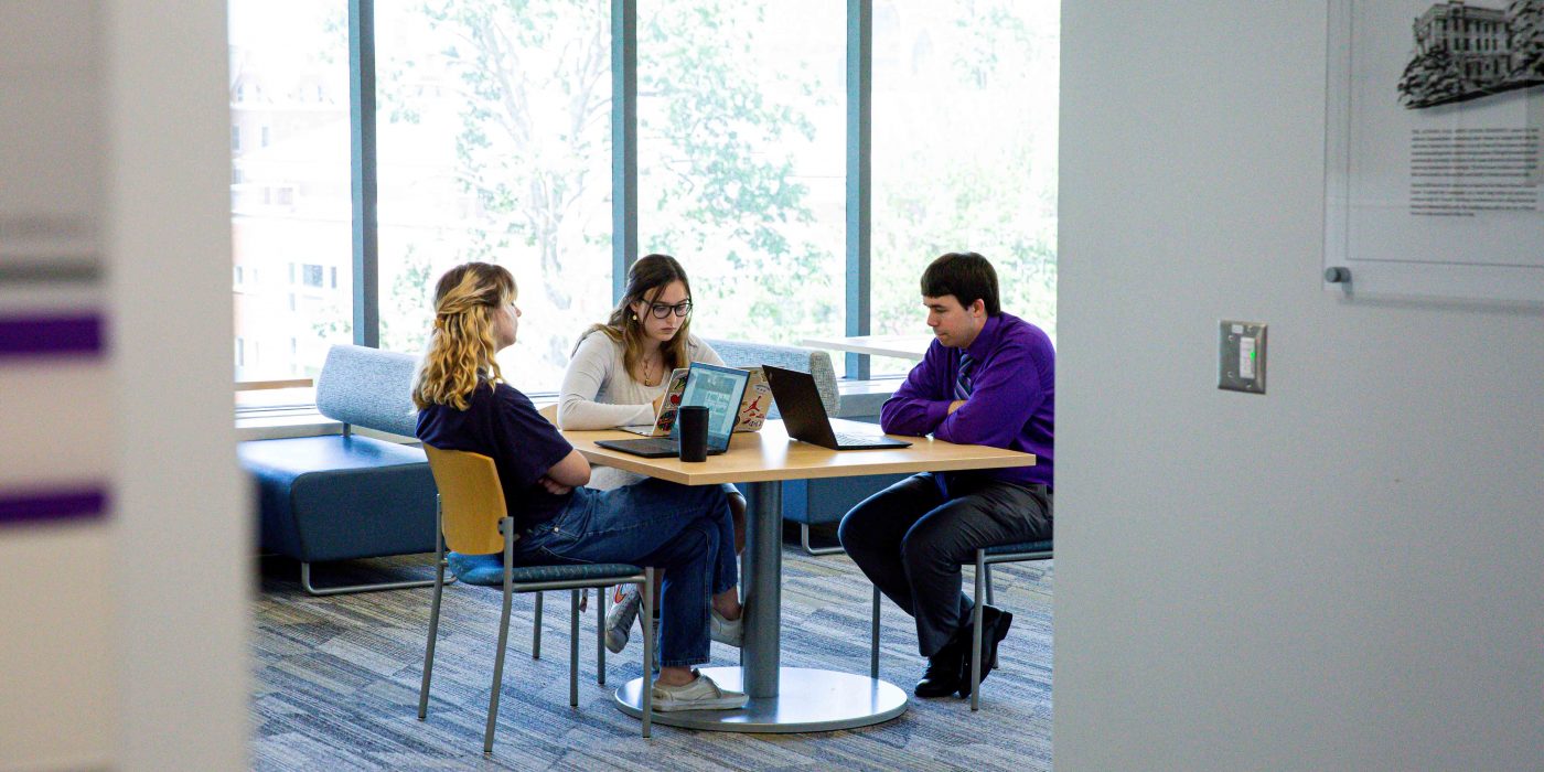Emma Jobe (left) and Ashley Mink discuss their research with Assistant Professor of Statistics Tyler George.