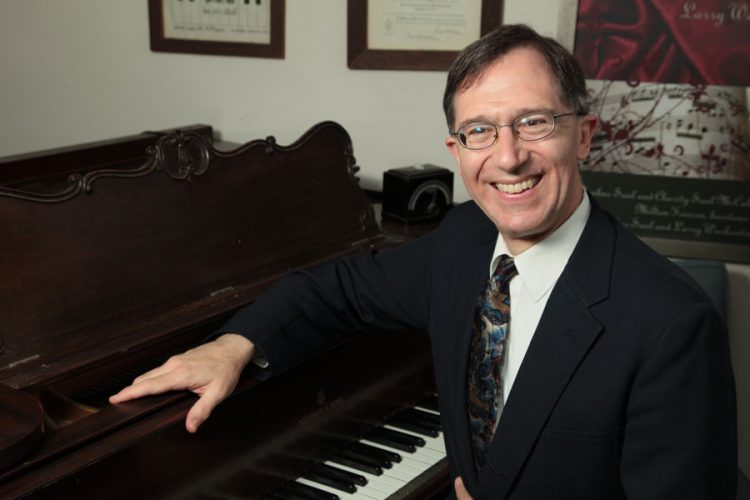 Composer-pianist Walter Saul sits at a grand piano.