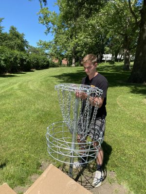 Maxwell Lundt installs a disc golf basket
